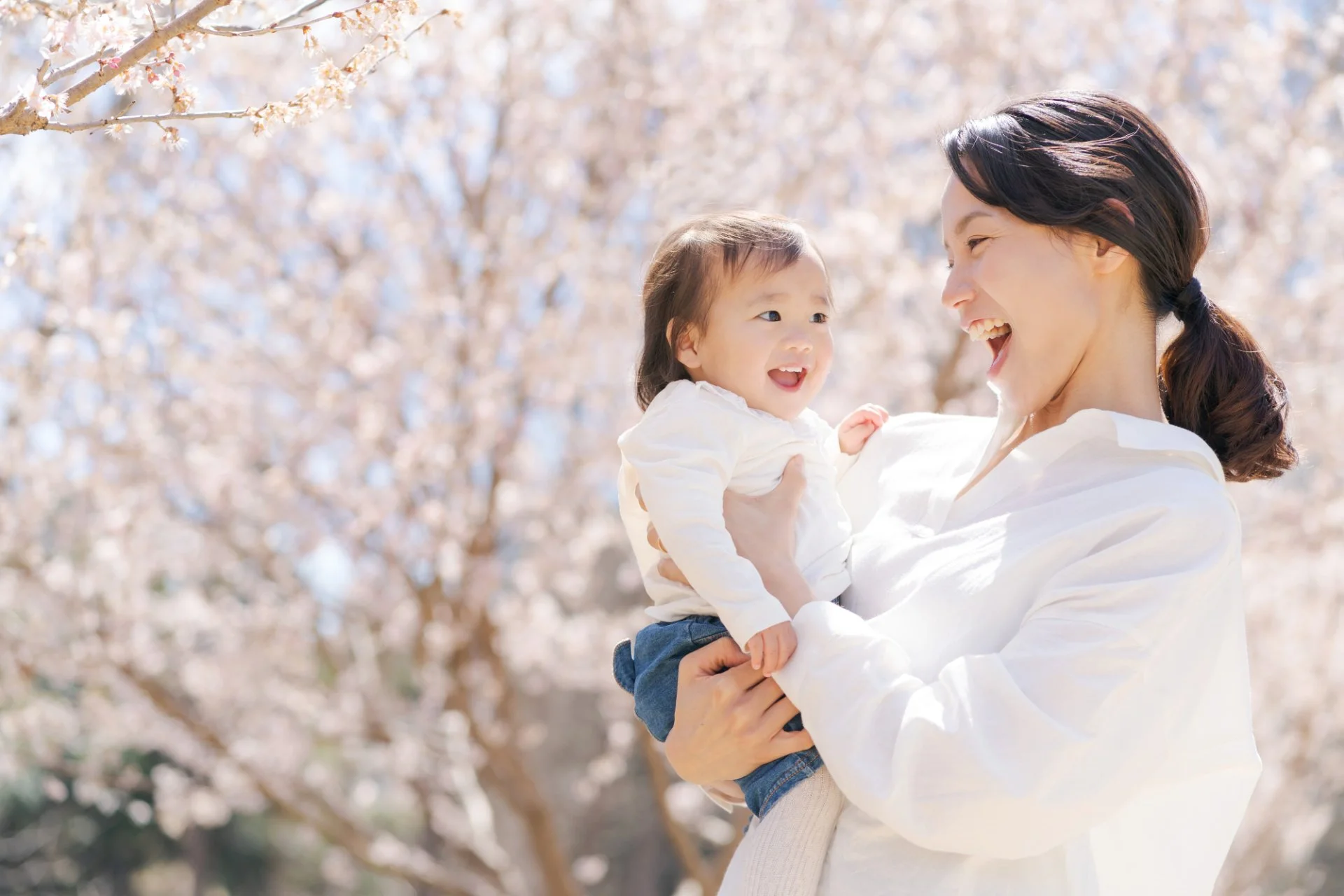 桜の木の下で赤ちゃんを抱いて笑い合う母親