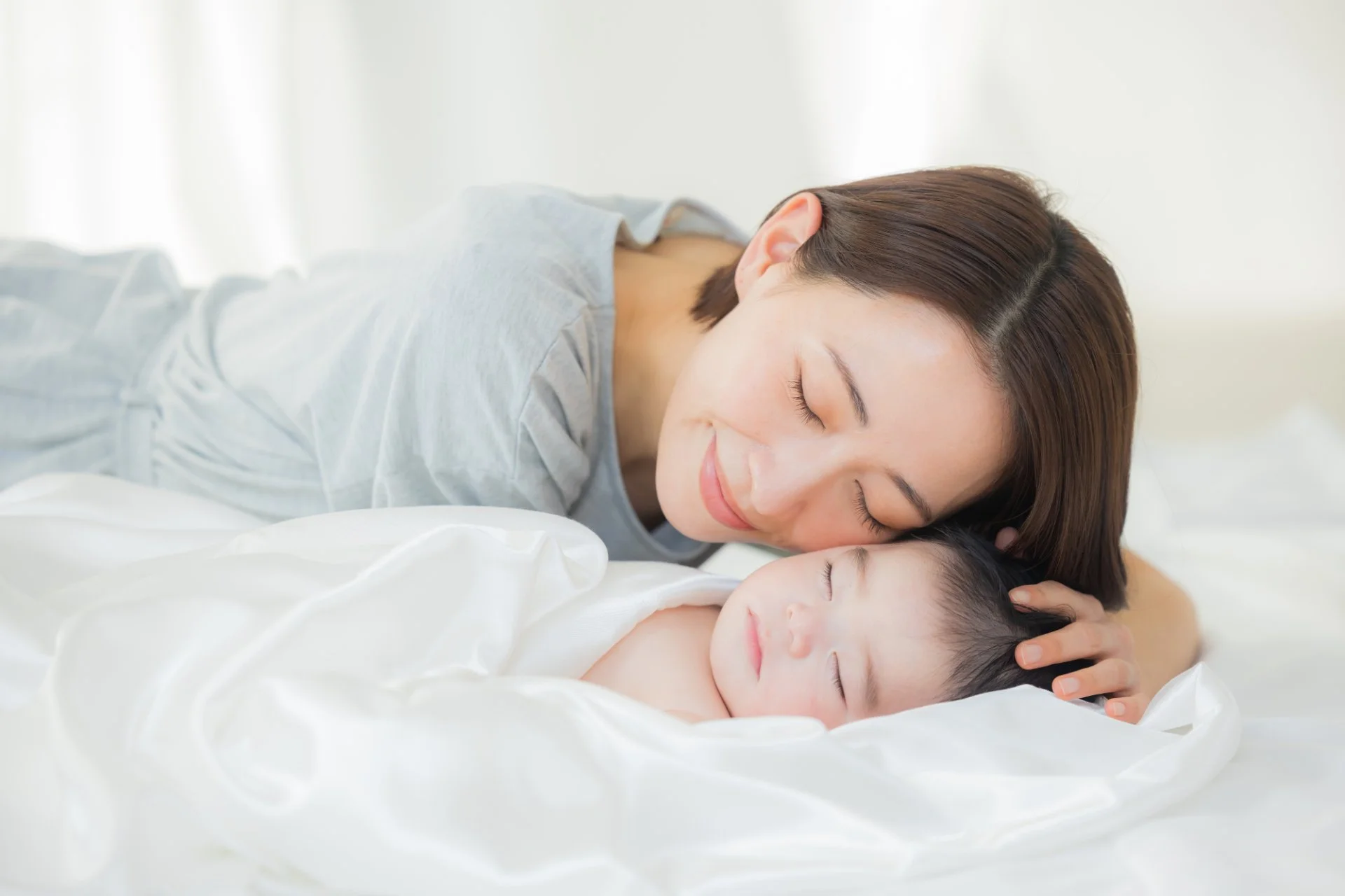 ベッドで眠る赤ちゃんに寄り添う母親
